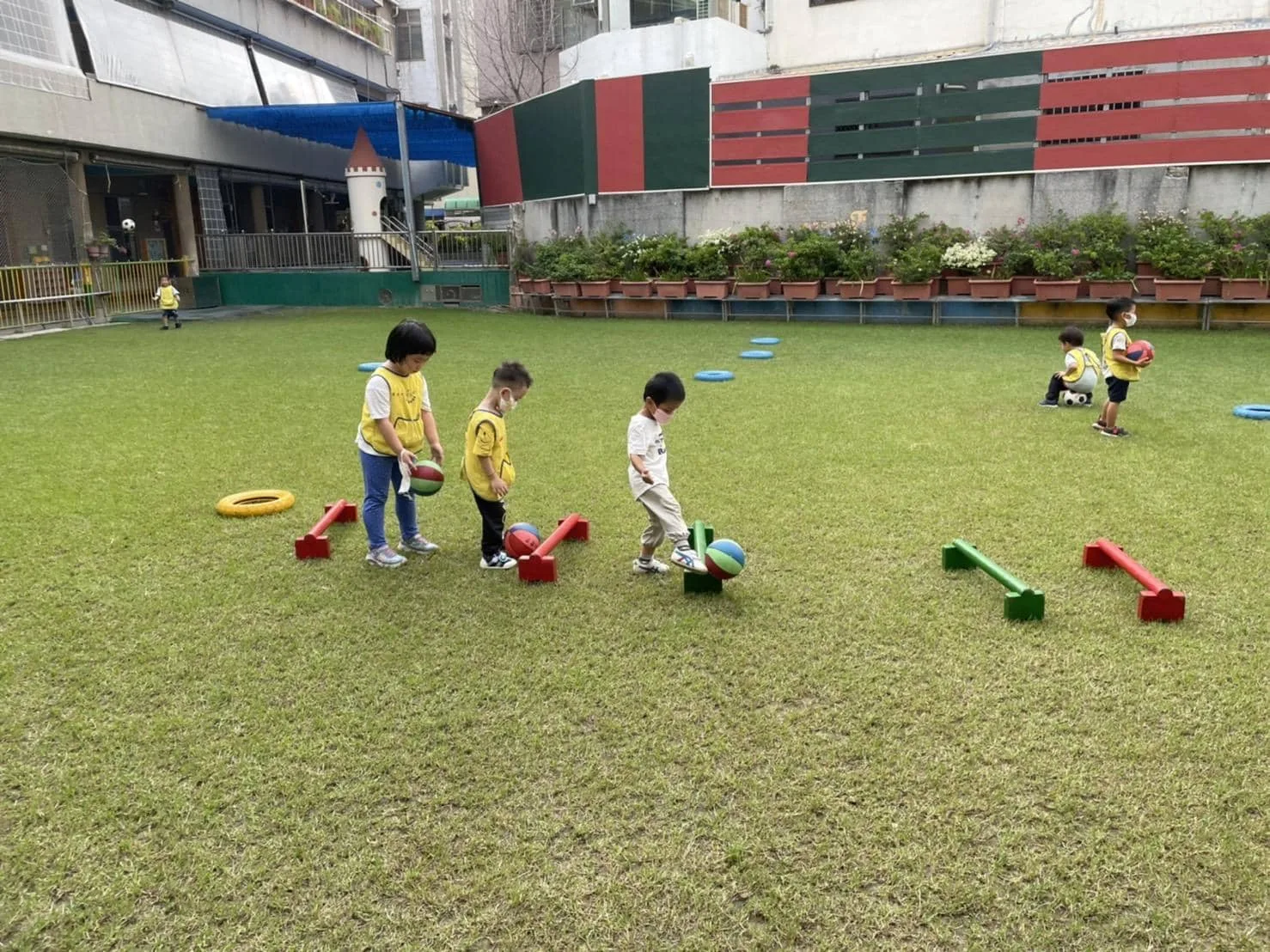 幼兒在草地上進行短平衡木與球類綜合體能遊戲